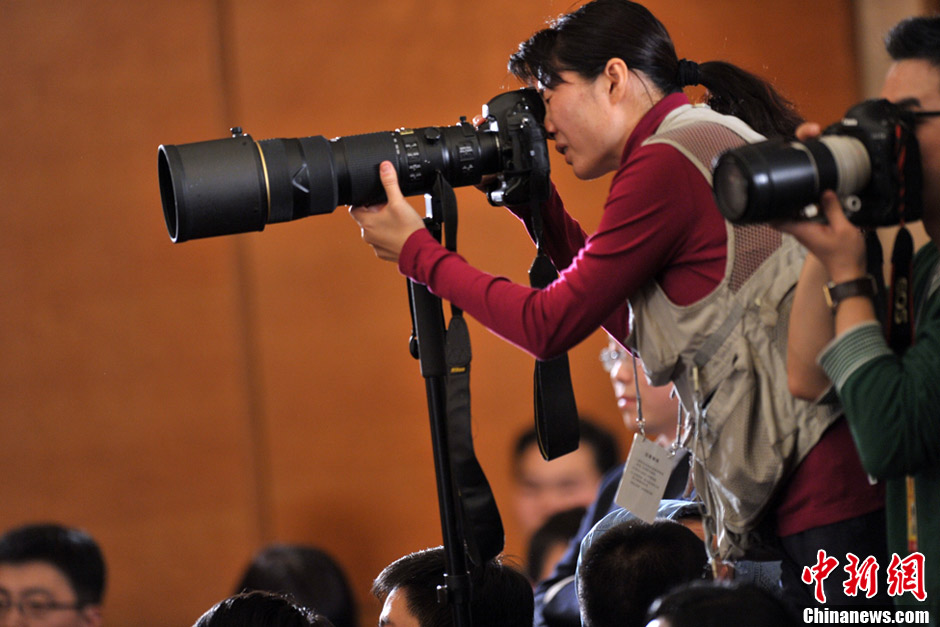 A female journalist covering the NPC and CPPCC sessions takes photos. (Photo/CNS)