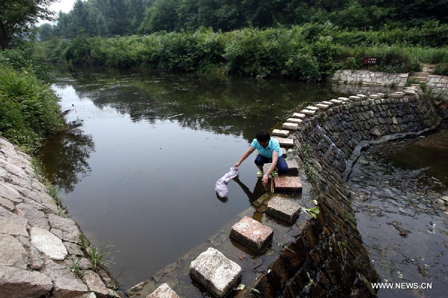 A villager cleans clothes by the riverside in the Haotang Village of Xinyang City, central China's Henan Province, June 20, 2013. (Xinhua/Li Mingfang) 