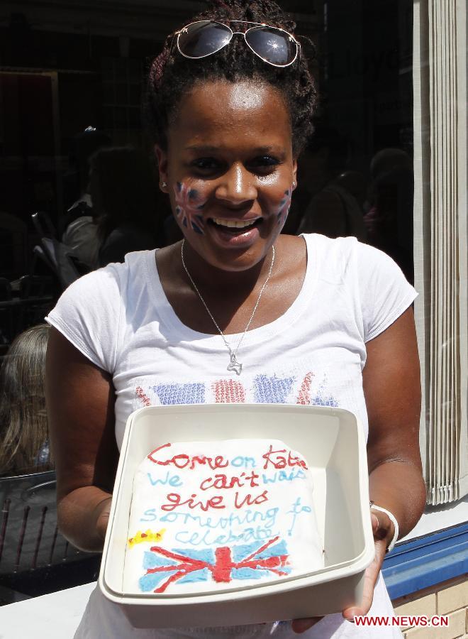 A royal fan poses for a photo with a cake outside the Lindo Wing of St. Mary's Hospital in London, July 22, 2013. The nation awaits news of a new royal baby. The nation awaits news of a new royal baby as Prince William's wife Kate has gone into labour and been admitted to St. Mary's Hospital for the birth of the couple's first child. (Xinhua/Yin Gang)